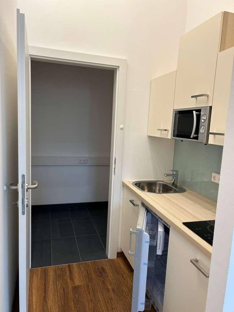 Kompakte Küchenzeile mit Spüle, Kochfeld und Mikrowelle, ideal für kleine Büros oder Apartments.