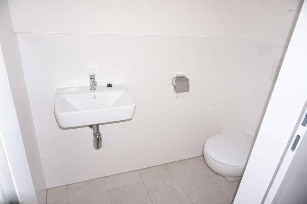 Modernes Gäste-WC mit weißem Waschbecken, wandhängender Toilette und hellen Fliesen an Wänden und Boden.