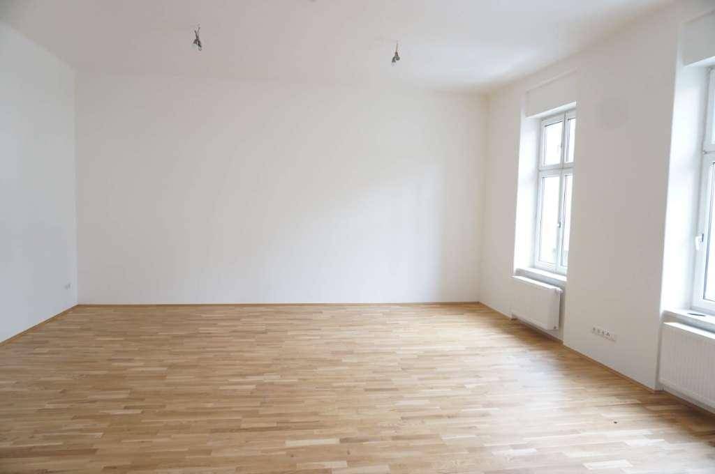 Geräumiger, leerer Raum mit hellem Parkettboden und zwei hohen Fenstern, ideal für Wohn- oder Schlafzimmer.