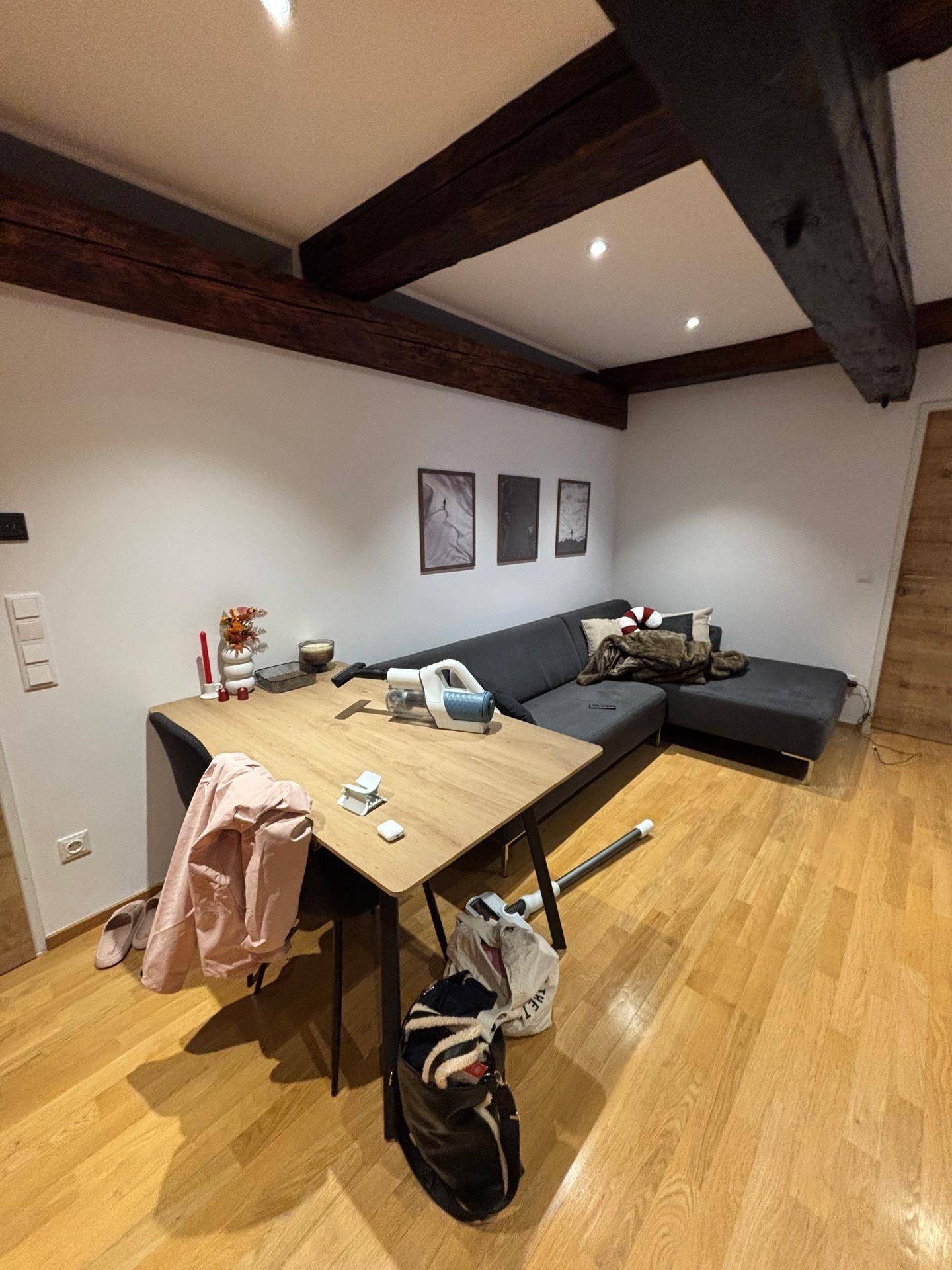 Wohnzimmer mit bequemer Eckcouch, Esstisch und charakteristischen Holzbalken, die den Raum prägen.