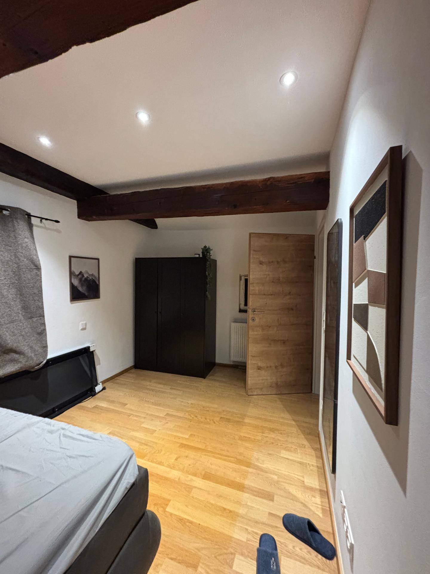 Helles Schlafzimmer mit Holzboden, dunklem Kleiderschrank und rustikalen Holzbalken an der Decke.