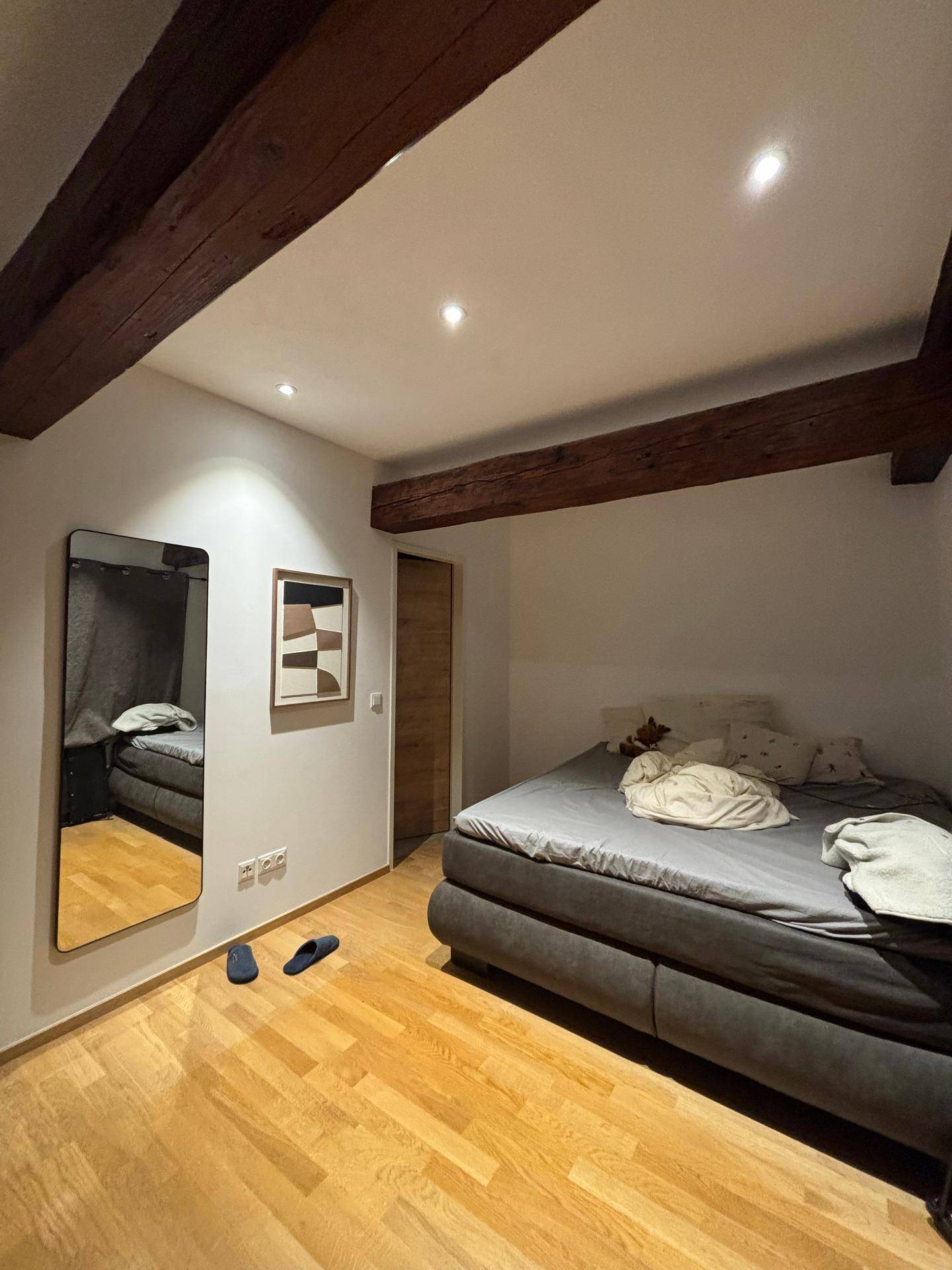 Gemütliches Schlafzimmer mit Holzbalken, Holzboden und einem großen Bett, ergänzt durch einen Wandspiegel.