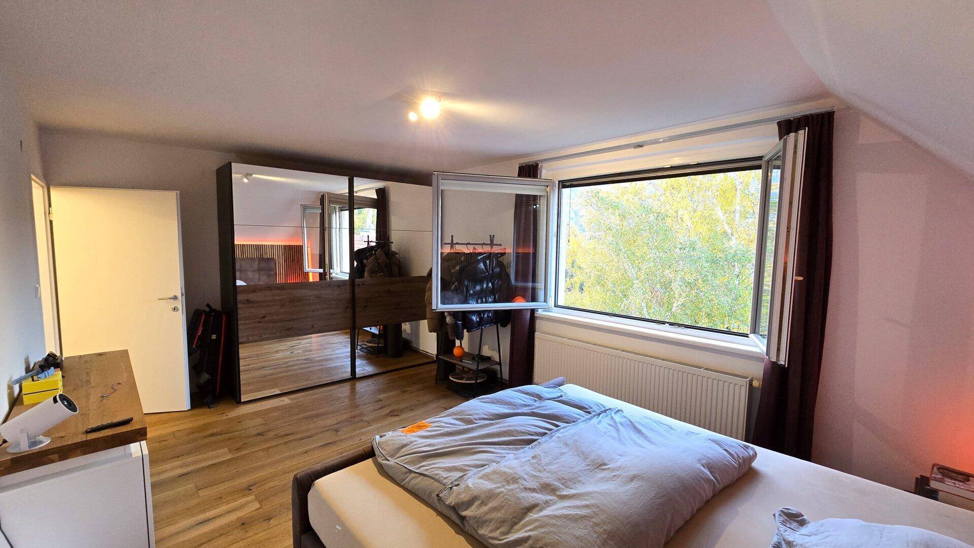 Helles Schlafzimmer mit großem Spiegelschrank und Blick ins Grüne durch das Fenster.