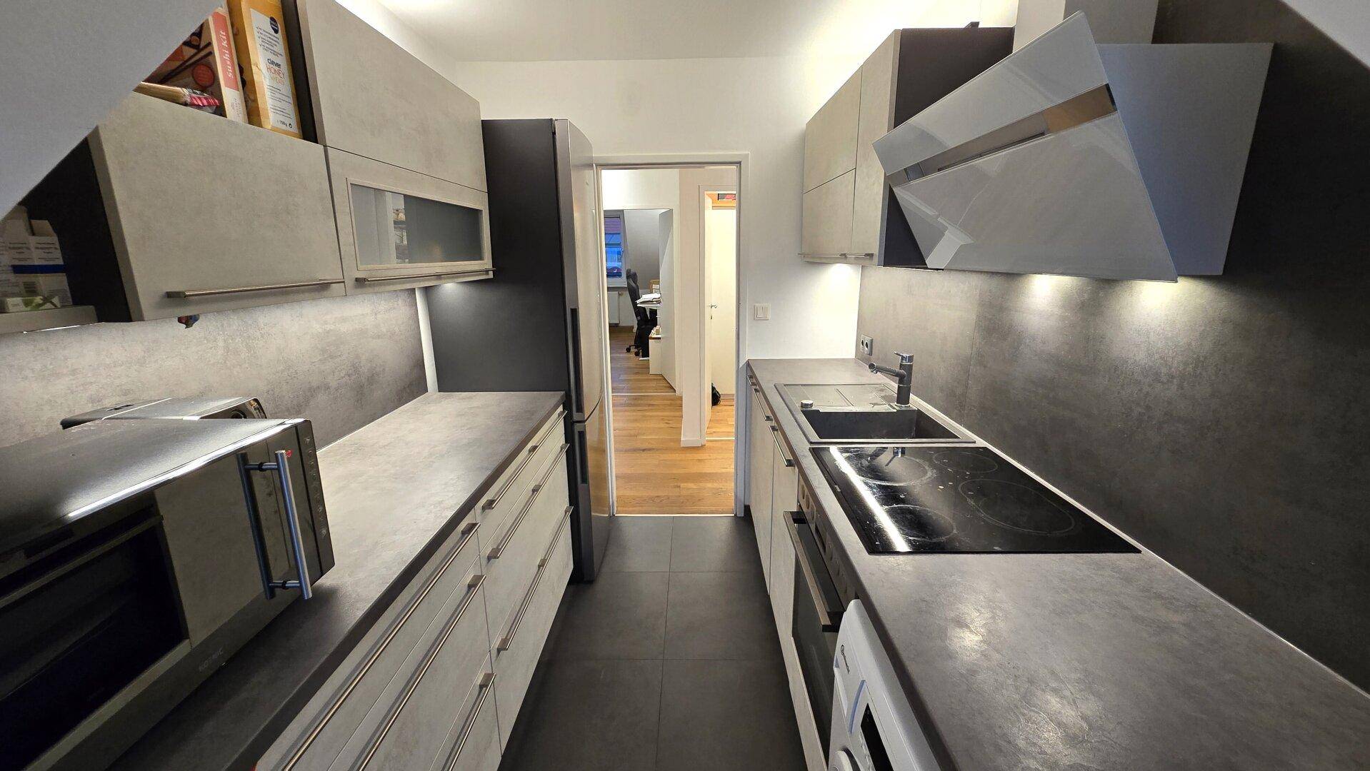 Moderne Küche mit grauen Fronten, integrierten Geräten und Blick in den Flur.