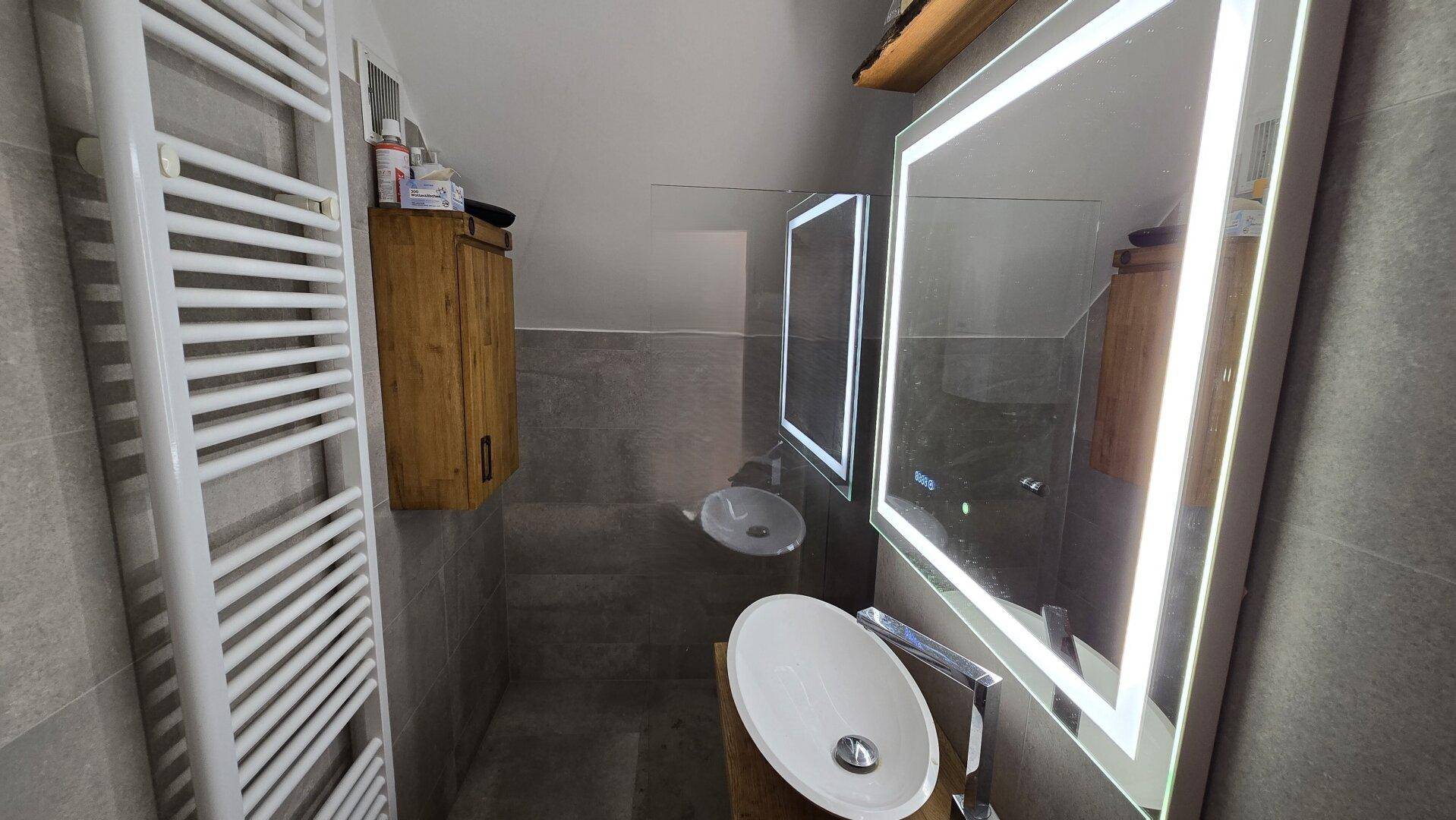 Modernes Badezimmer mit beheiztem Handtuchhalter, Aufsatzwaschbecken und beleuchtetem Spiegel.