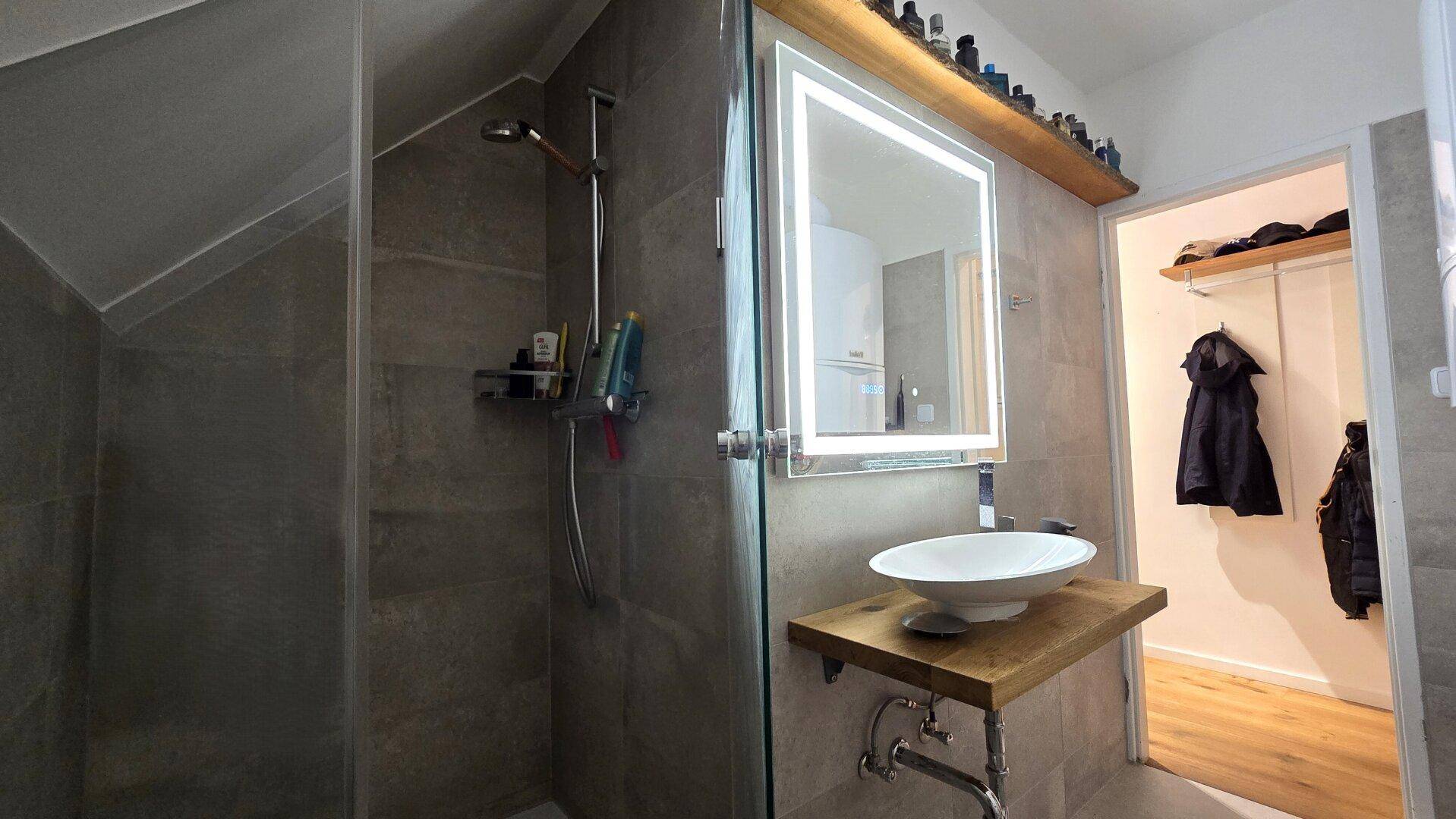 Modernes Badezimmer mit begehbarer Dusche, Aufsatzwaschbecken und beleuchtetem Spiegel im Dachgeschoss.