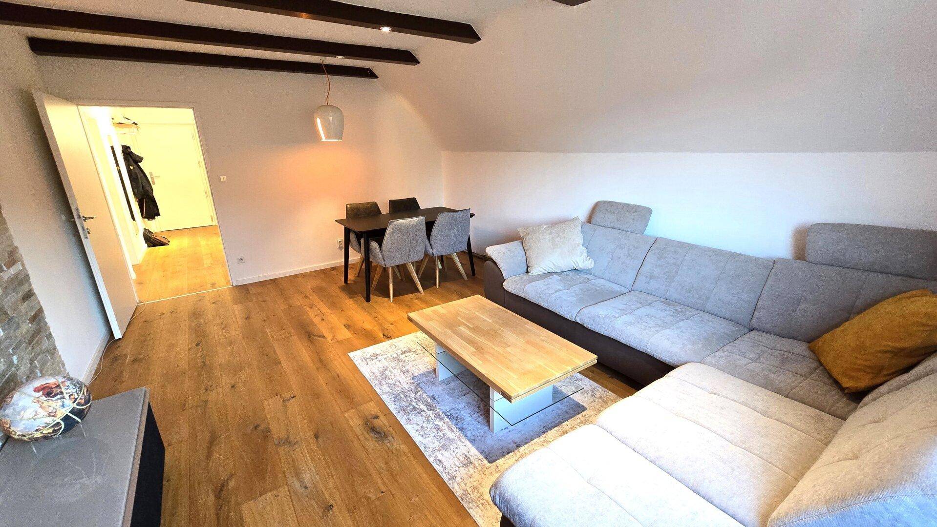 Gemütlicher Wohn-Essbereich im Dachgeschoss mit Holzbalken und modernem Sofa.