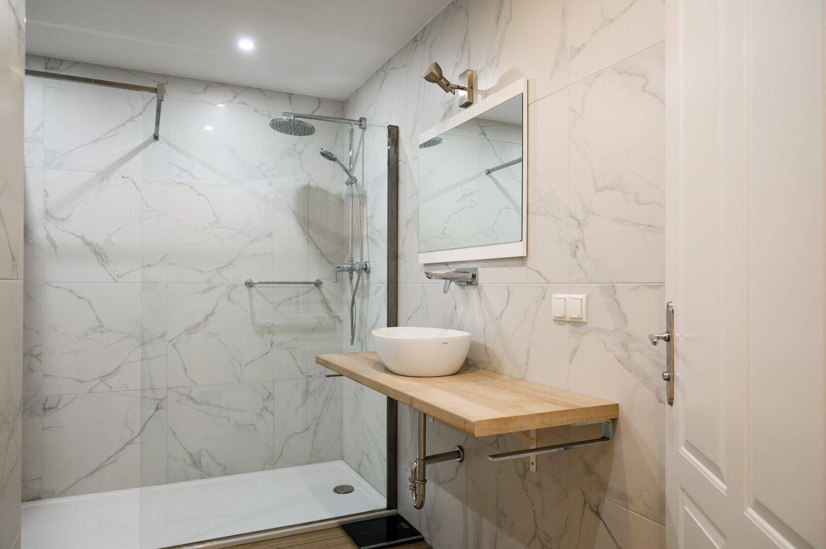 Modernes Badezimmer mit Marmoroptik-Fliesen, begehbarer Dusche und Einzelwaschbecken auf Holzplatte.