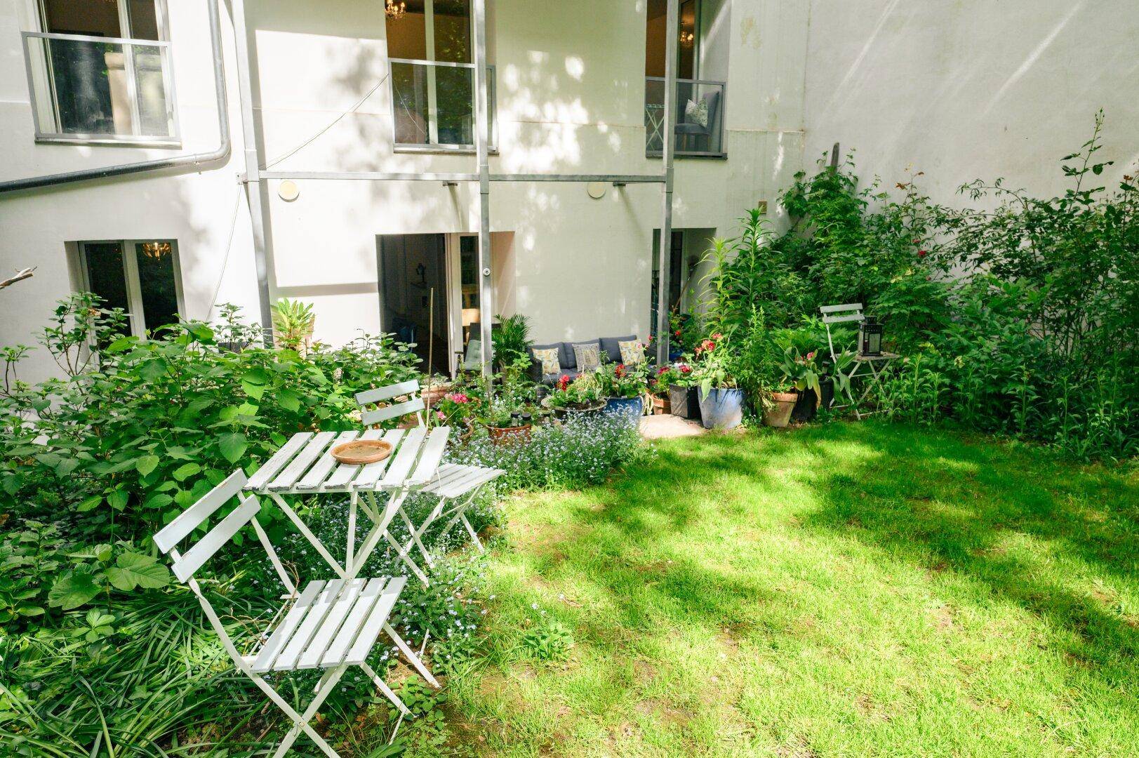 Gartenbereich mit Rasenfläche und kleiner weißer Sitzgruppe vor der hellen Gebäudefassade.