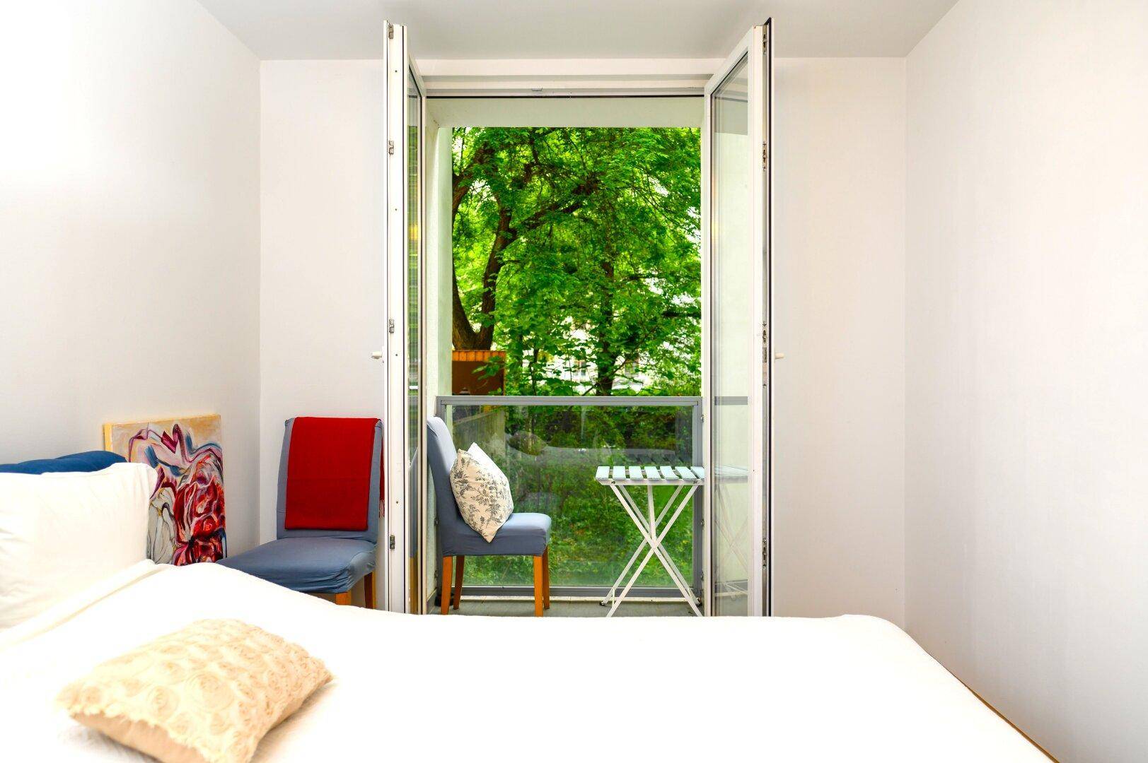 Schlafzimmer mit Bett und offenem Zugang zu einem Balkon mit Blick ins Grüne.