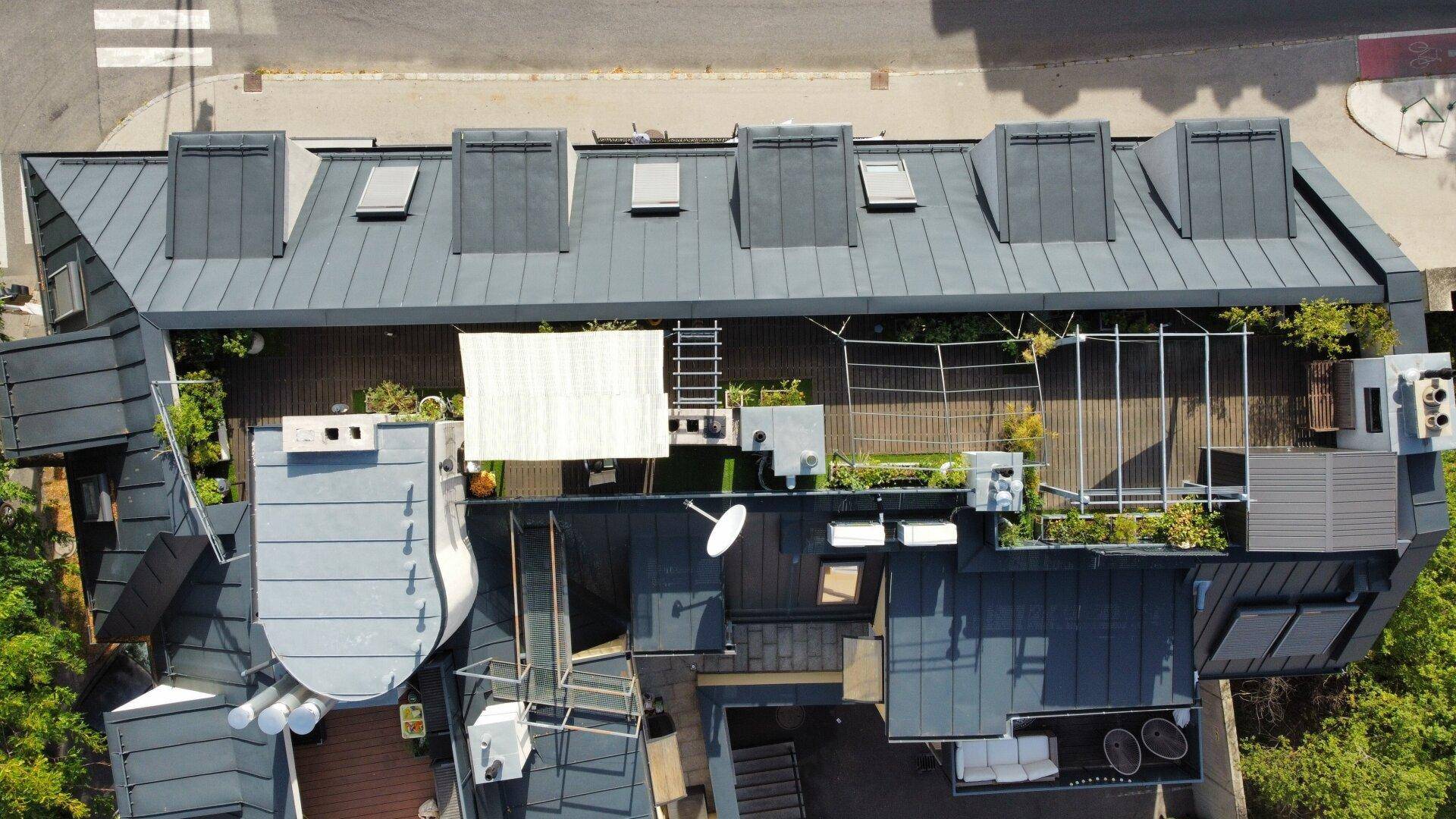 Luftaufnahme des Gebäudes mit großer Dachterrasse und umliegenden Dächern.