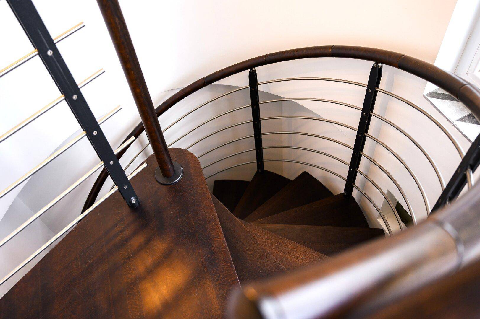 Elegante Wendeltreppe mit Holzstufen und Metallgeländer verbindet die Ebenen.