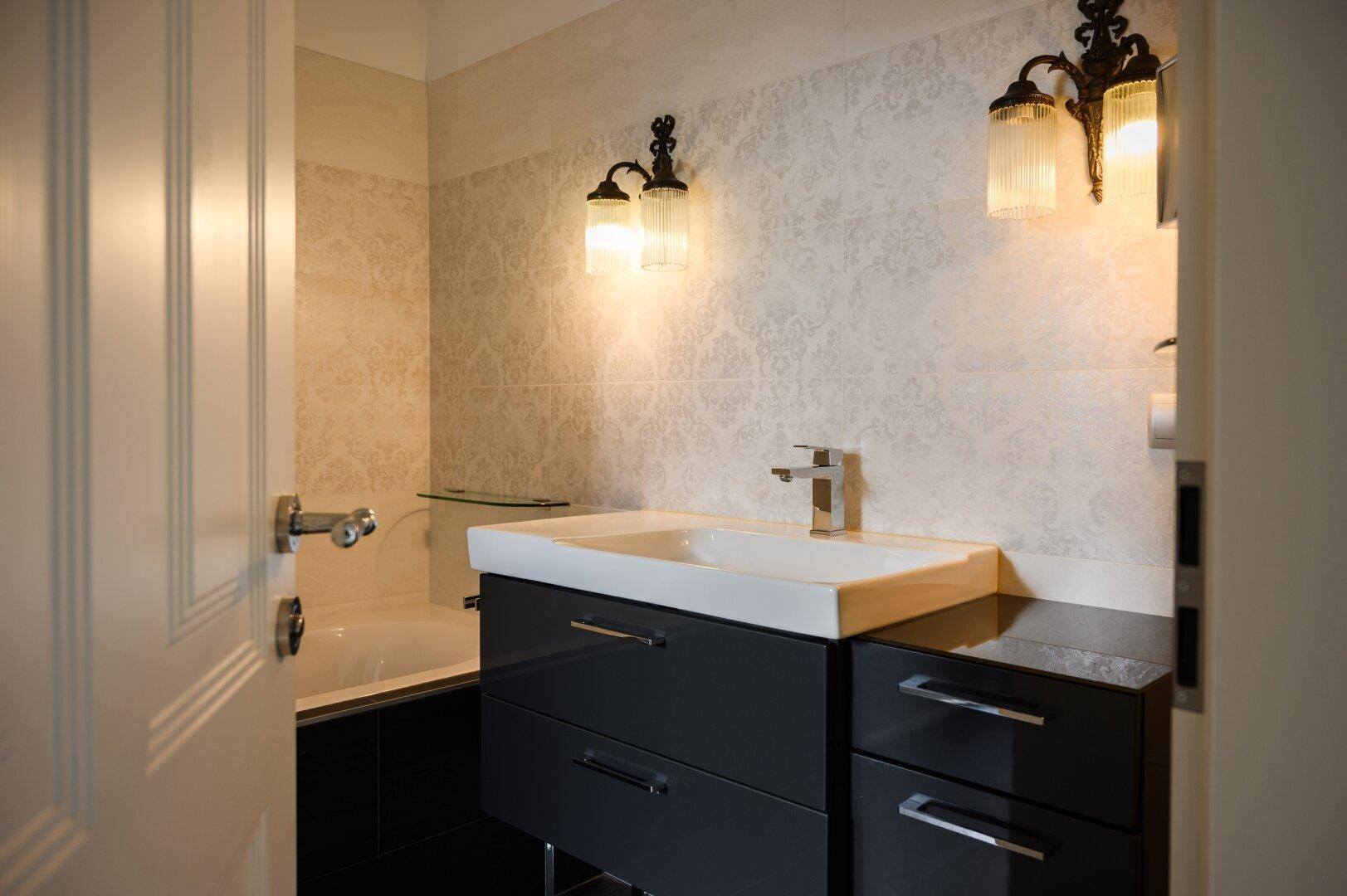 Modernes Badezimmer mit Waschtisch, Badewanne und stilvollen Wandleuchten.