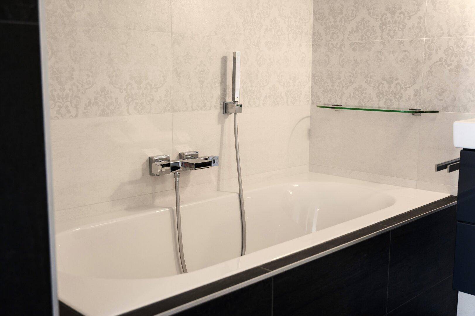 Eingebaute Badewanne mit moderner Armatur und hellen Fliesen an der Wand.