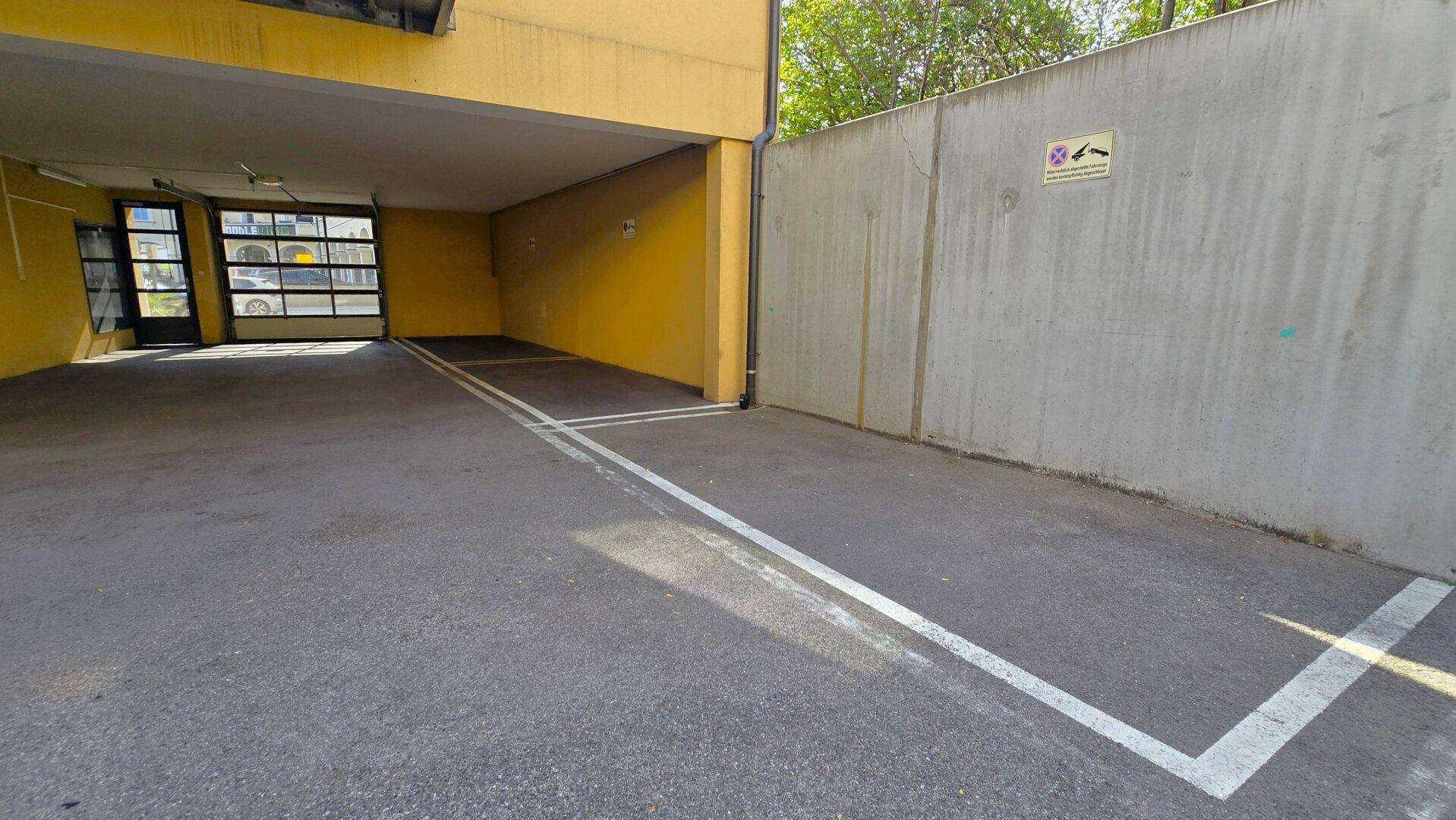 Außenparkplatz vor einer Garage mit gelber Fassade und Betonwand.