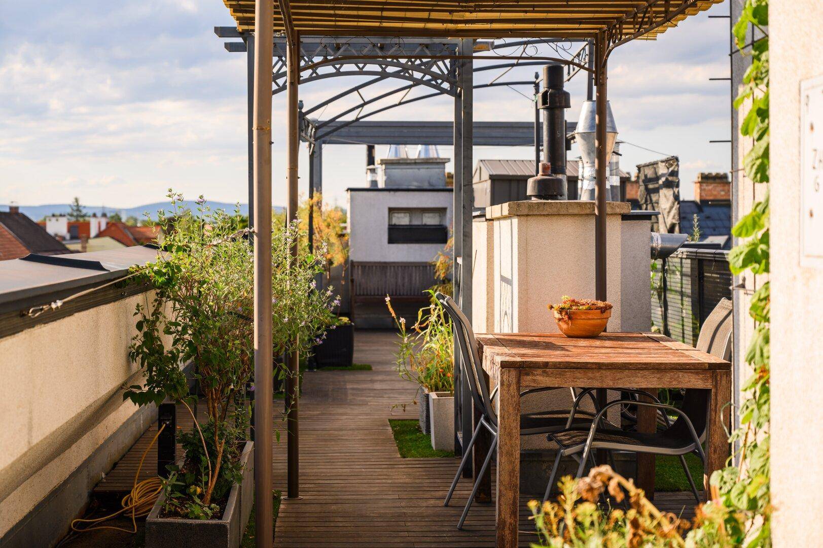 Geräumige Dachterrasse mit Holzbelag, Gartenmöbeln und Pflanzen, ideal für Entspannung im Freien.