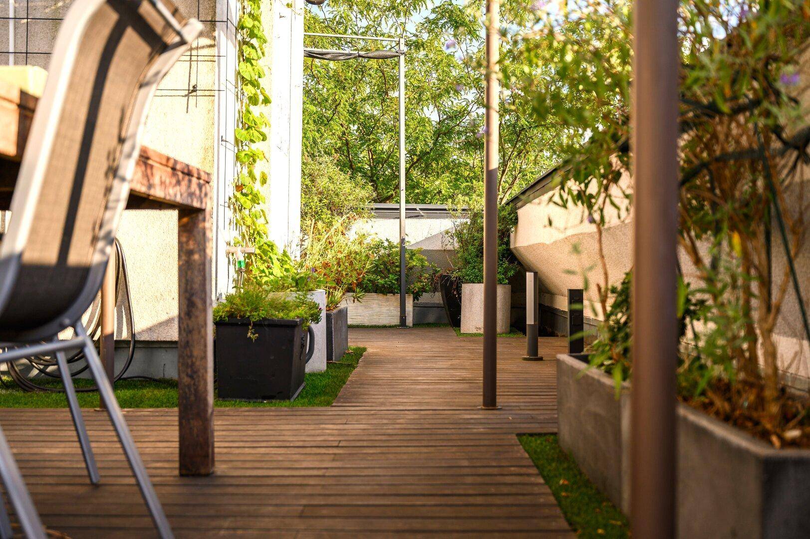 Teil einer Holzterrasse mit üppigen Topfpflanzen und viel natürlichem Licht, ideal zum Entspannen.