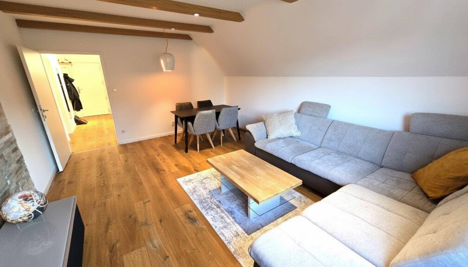 Geräumiger Wohn-Essbereich mit Holzbalken, Parkettboden und offenem Zugang zu einem weiteren Raum.