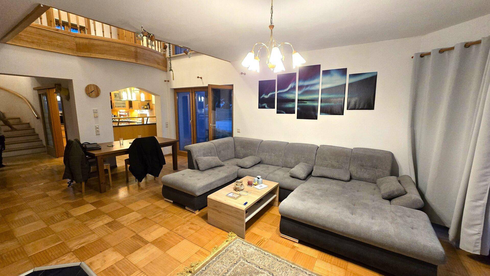 Offener Wohn-Essbereich mit großem Sofa, Esstisch und Blick auf die Treppe.