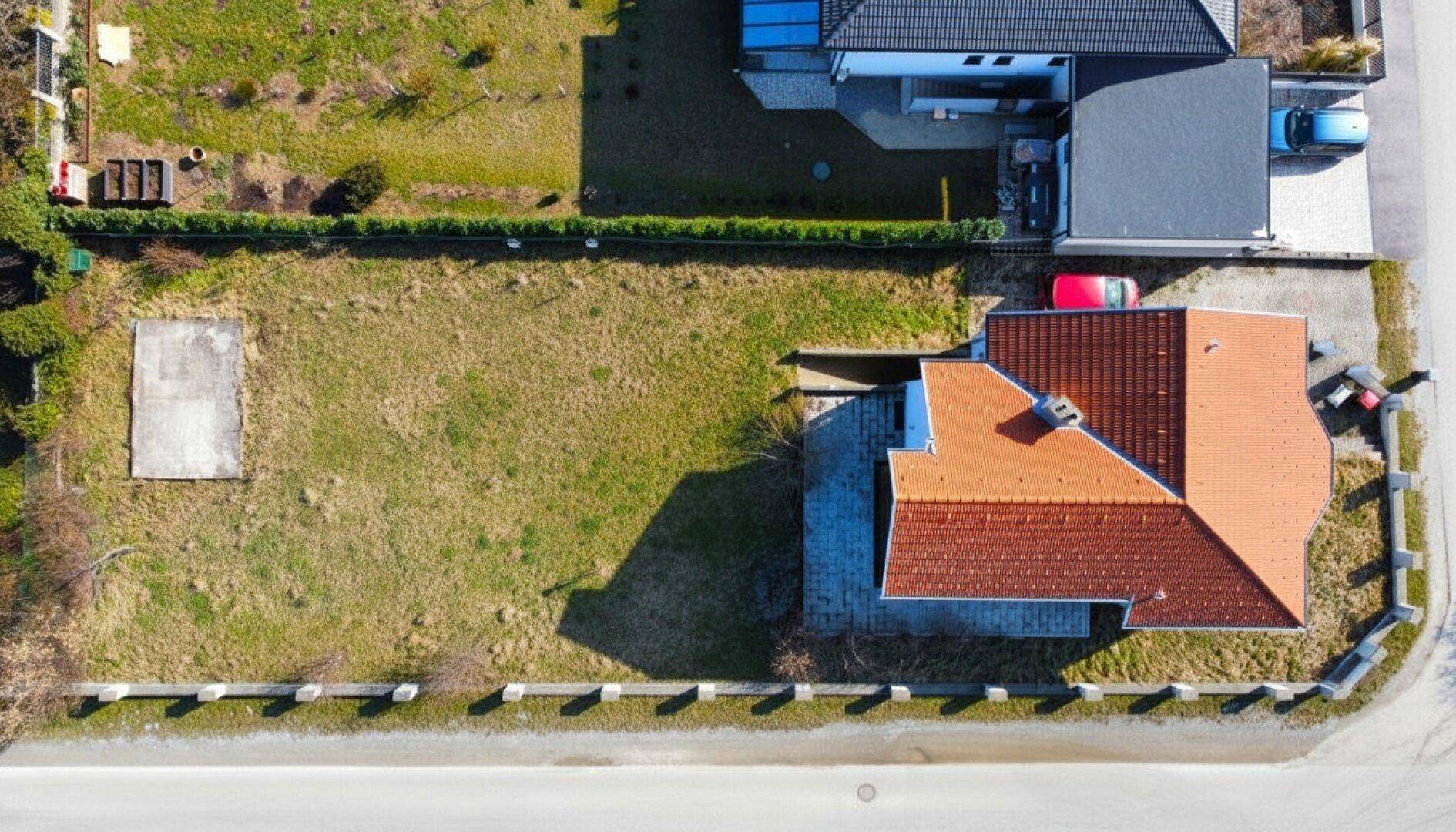 Draufsicht auf ein Einfamilienhaus mit rotem Dach und angrenzendem Grundstück.