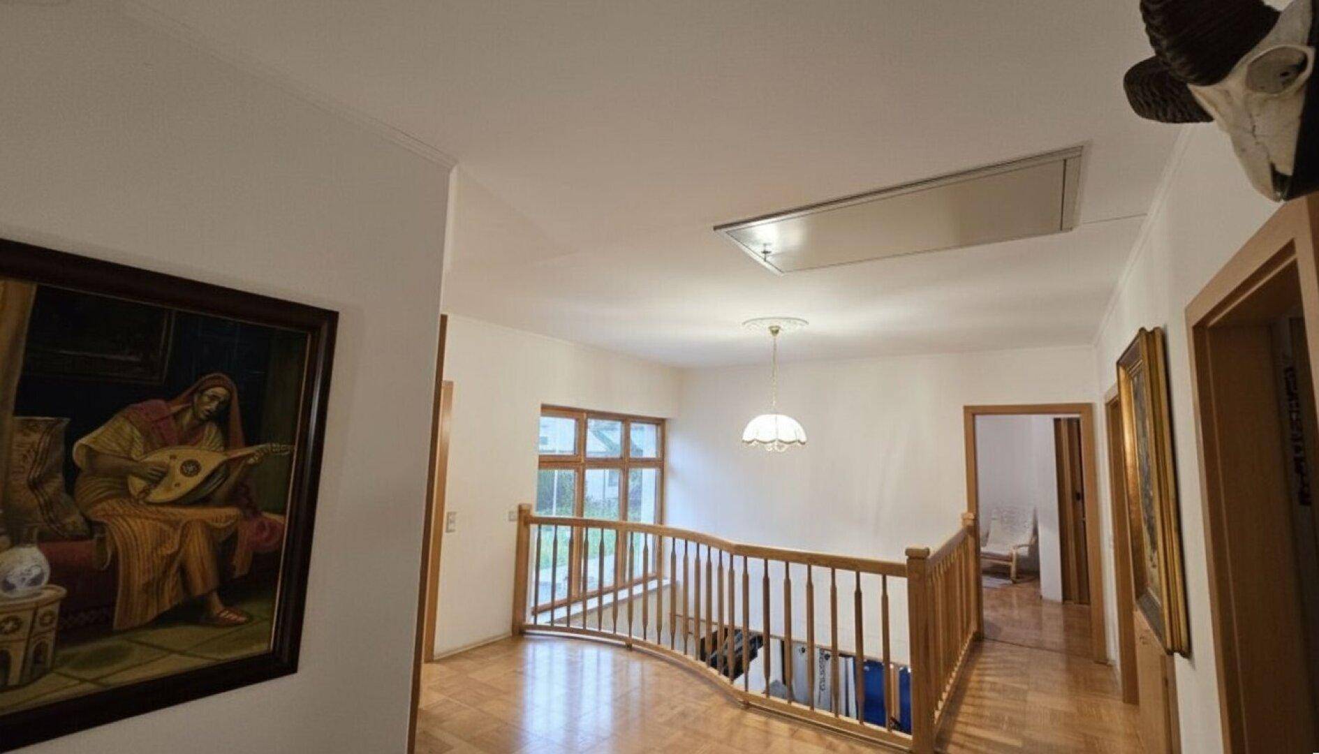 Geräumiger Flur im Obergeschoss mit Holzgeländer und dekorativen Gemälden an den Wänden.