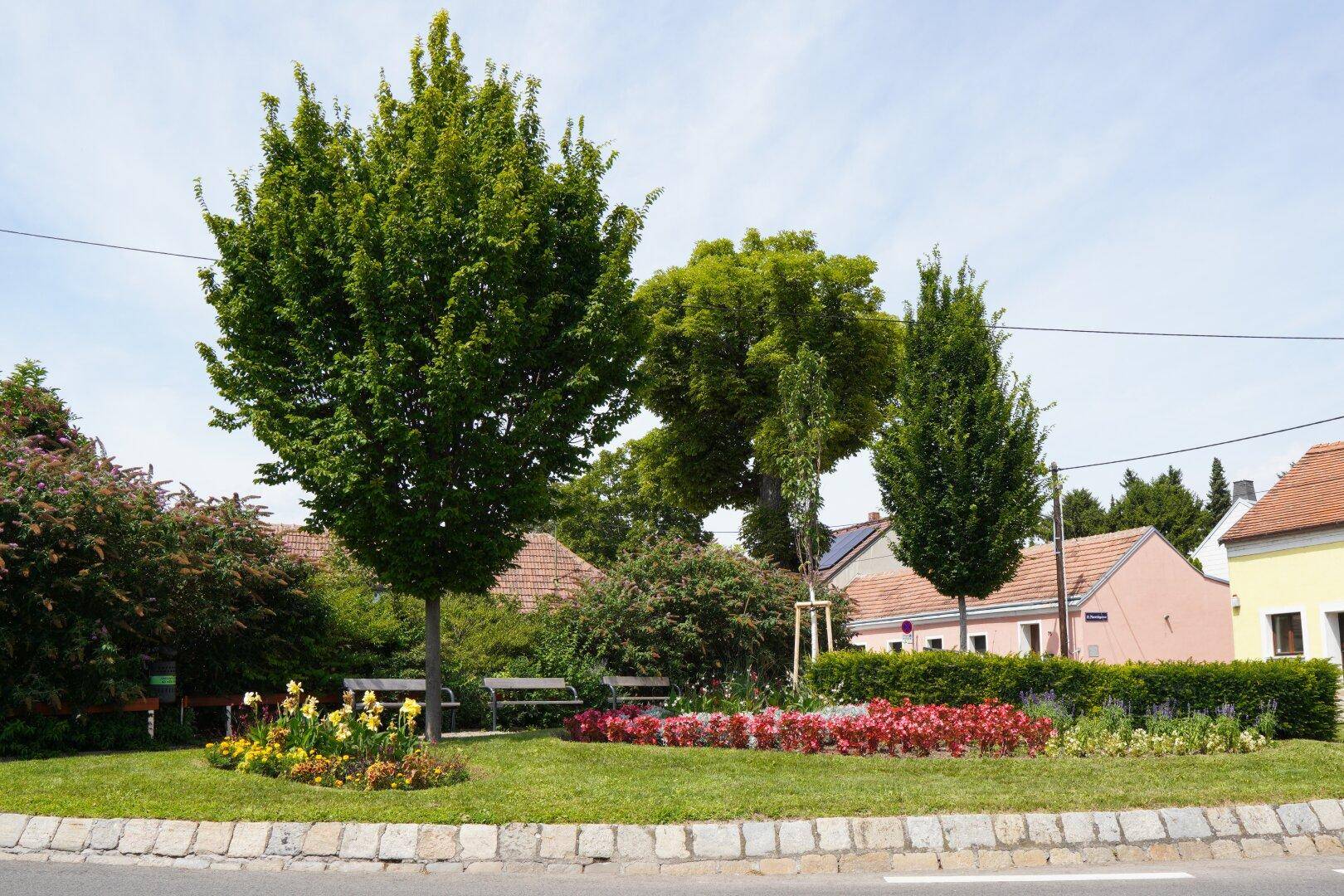 Grüne Umgebung mit Bäumen, Blumenbeeten und Wohnhäusern im Hintergrund.