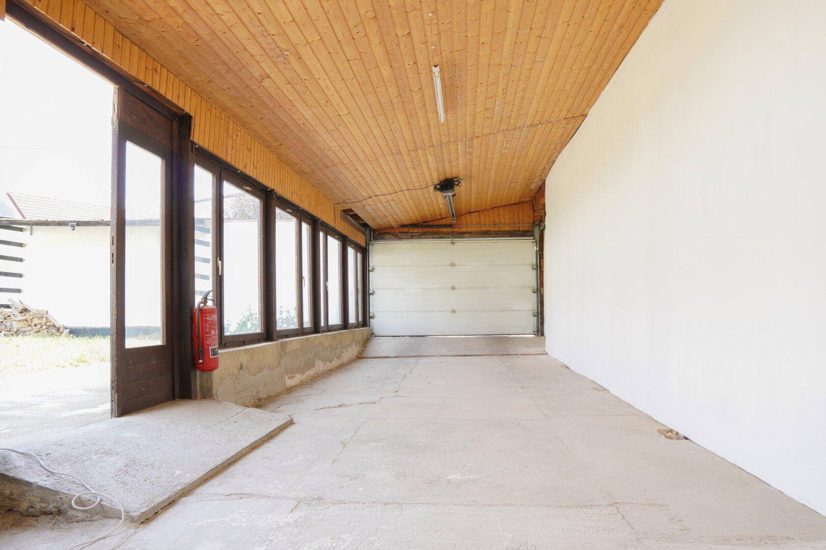 Geräumige Garage mit Betonboden, Holzdecke und Zugang nach außen.