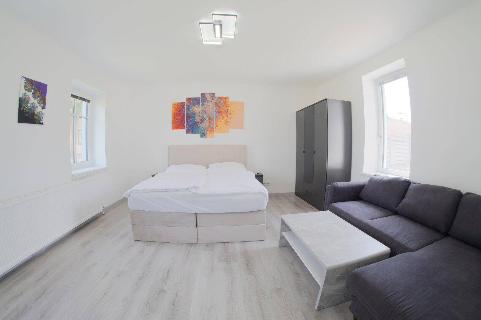 Helles Schlafzimmer mit Doppelbett, Sofa und modernem Kleiderschrank.