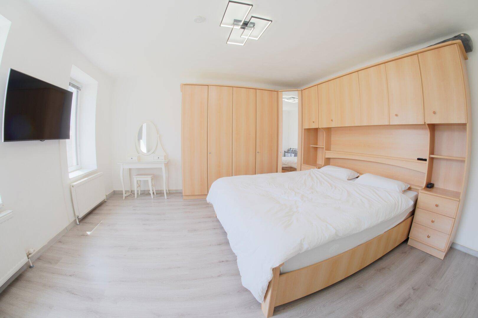 Schlafzimmer mit hellem Holzbett, integrierten Schränken und einem Schminktisch.