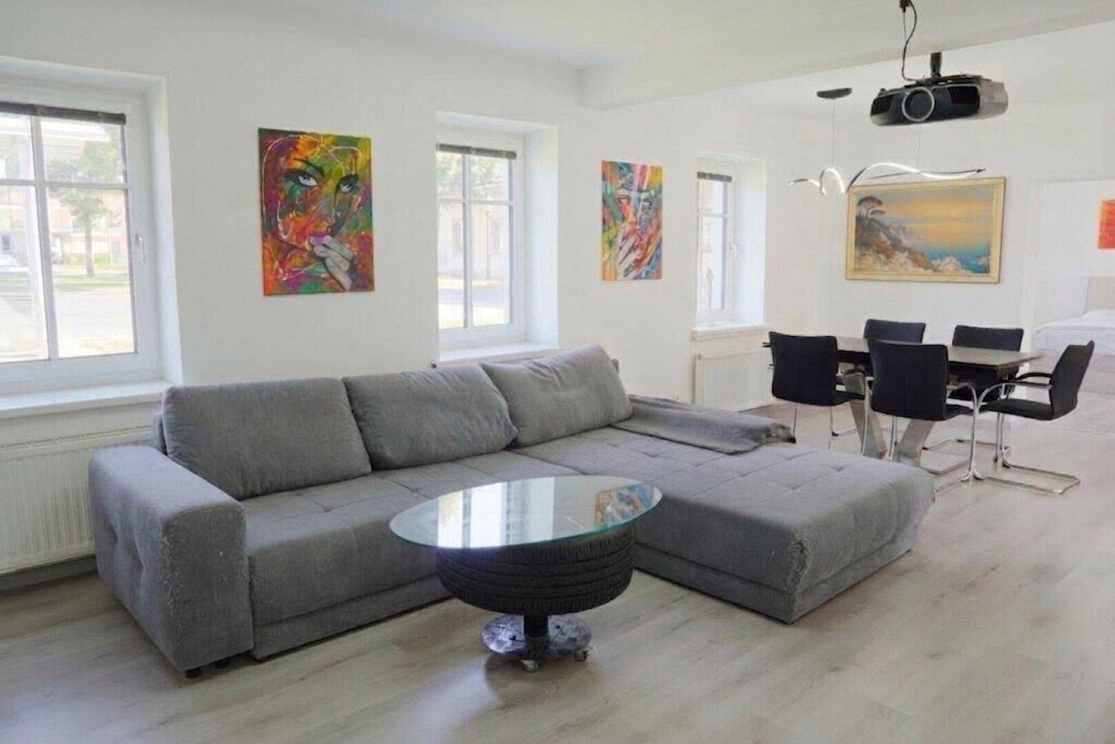Helles Wohn- und Esszimmer mit modernem Sofa, Esstisch und farbenfroher Kunst.