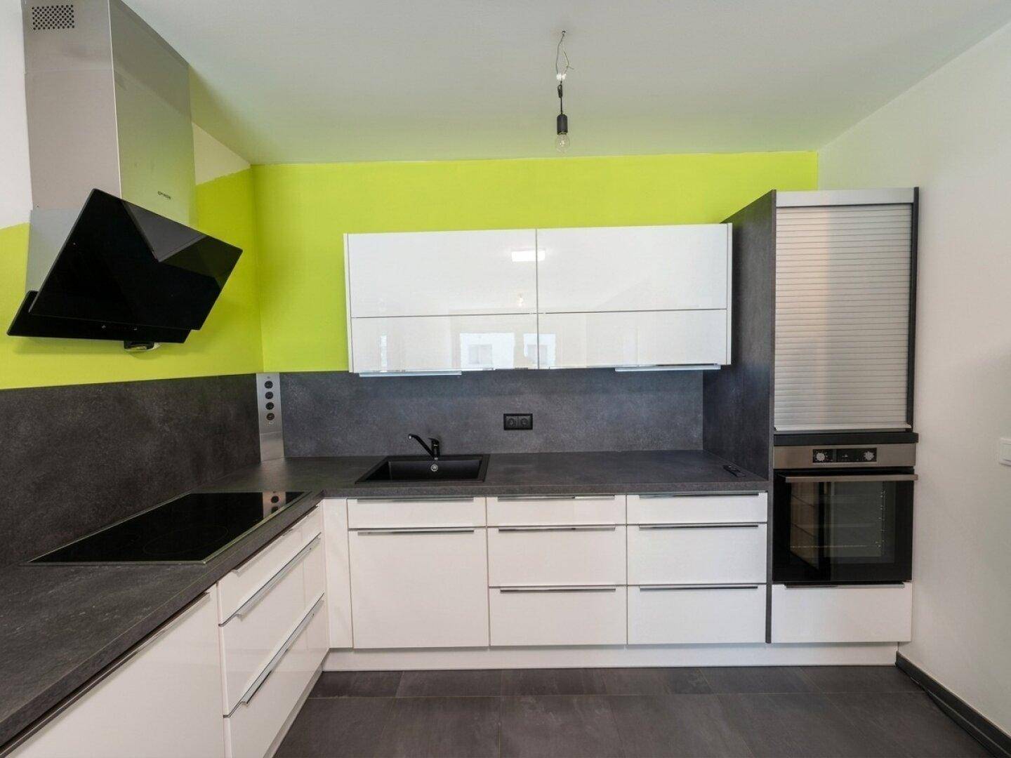 Moderne Küche mit weißen Hochglanzschränken, dunklen Arbeitsplatten und einer auffälligen grünen Wand.