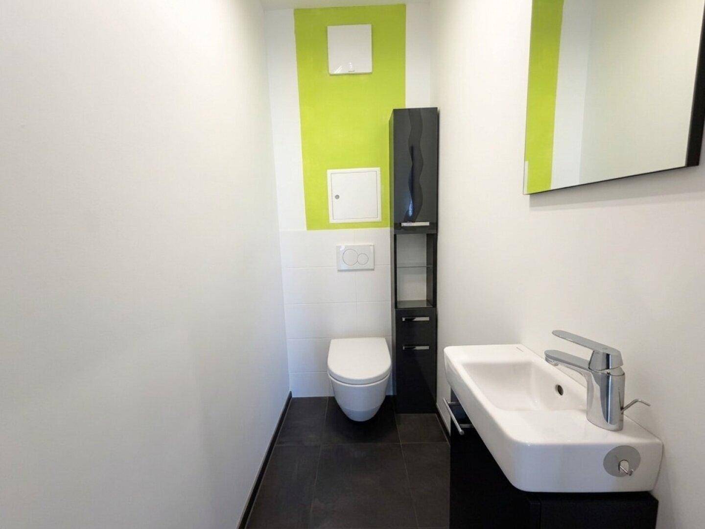Modernes Gäste-WC mit wandhängender Toilette, kleinem Waschbecken und grüner Akzentwand.