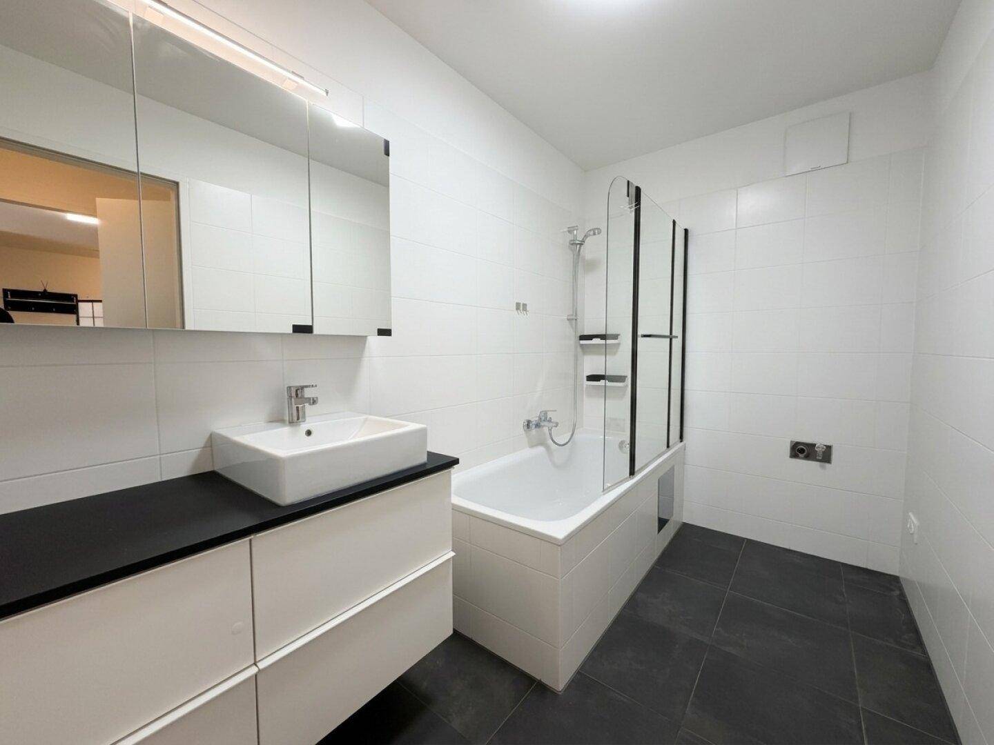 Helles Badezimmer mit Badewanne, Duschabtrennung, modernem Waschtisch und Spiegelschrank.