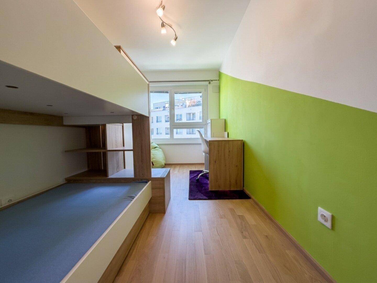 Kinder- oder Gästezimmer mit Hochbettkonstruktion, Schreibtisch und einer lebhaften grünen Wand.