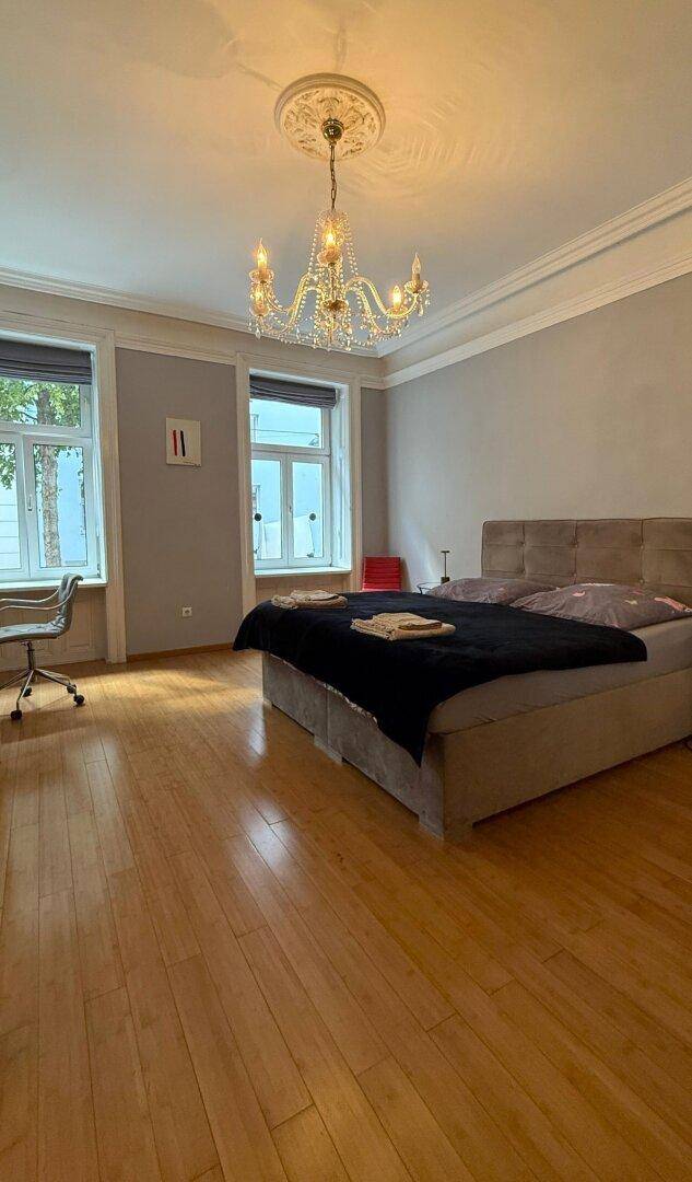Geräumiges Schlafzimmer mit Holzboden, Kronleuchter und hohen Decken.