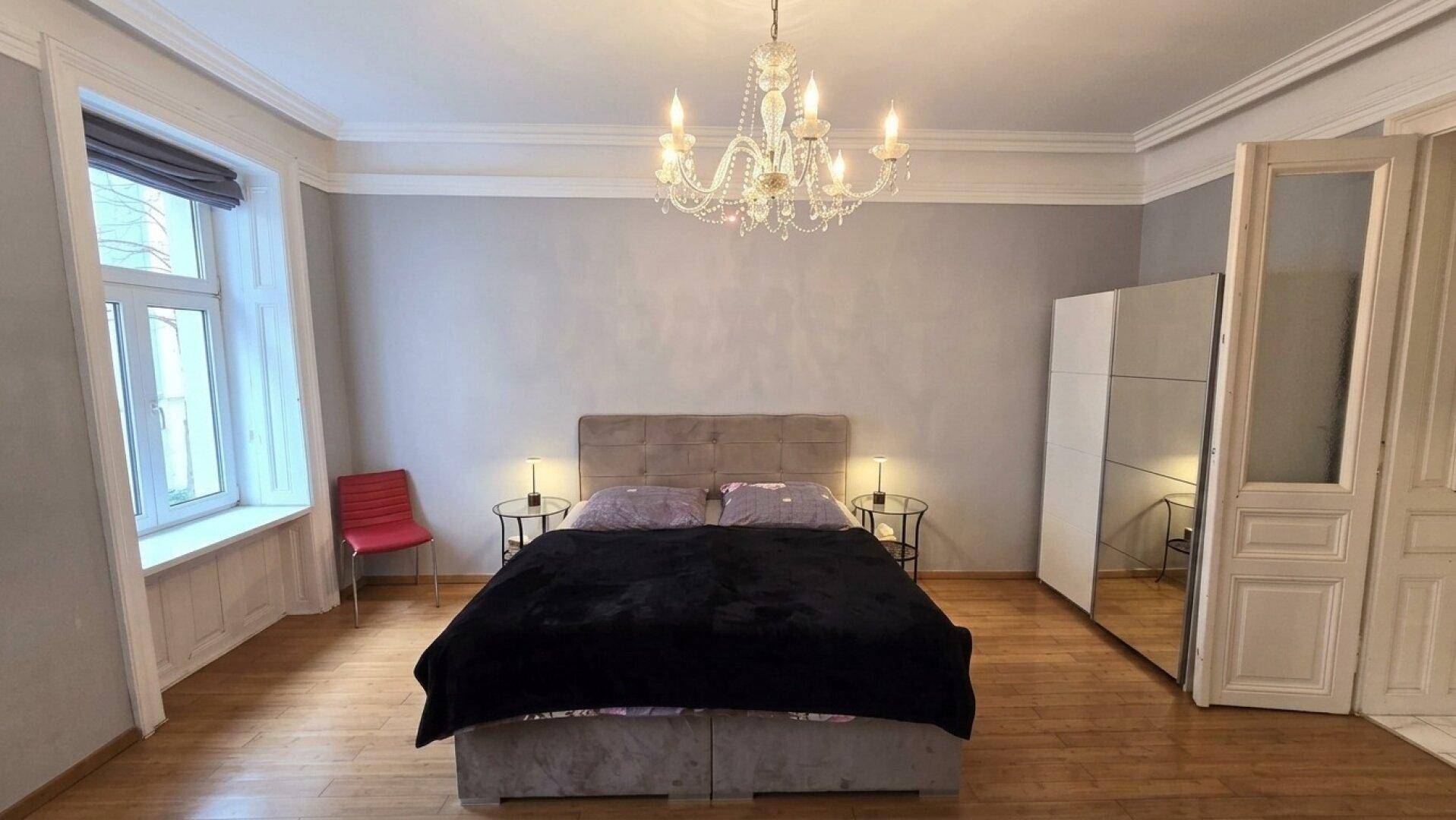 Helles Schlafzimmer mit Holzboden, Kronleuchter und großem Kleiderschrank.