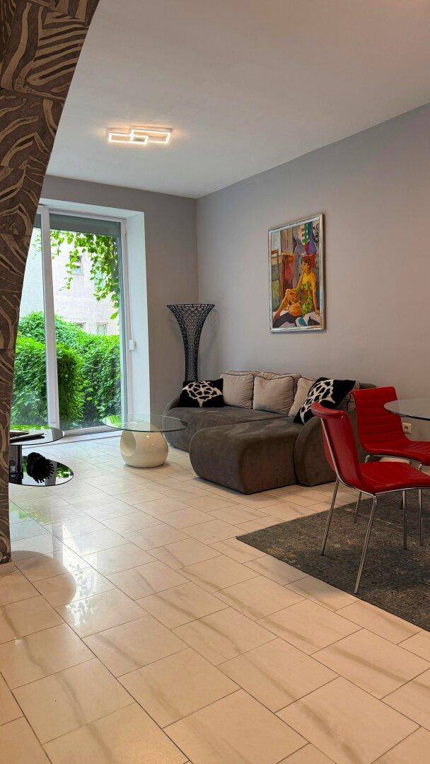 Helles Wohnzimmer mit Fliesenboden, bequemer Couch und Zugang zum Außenbereich.