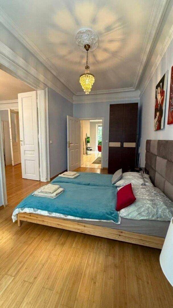 Helles Schlafzimmer mit Holzboden, Kronleuchter und Zugang zu weiteren Räumen.