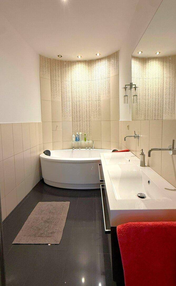 Helles Badezimmer mit Eckbadewanne, Doppelwaschbecken und dunklem Fliesenboden.