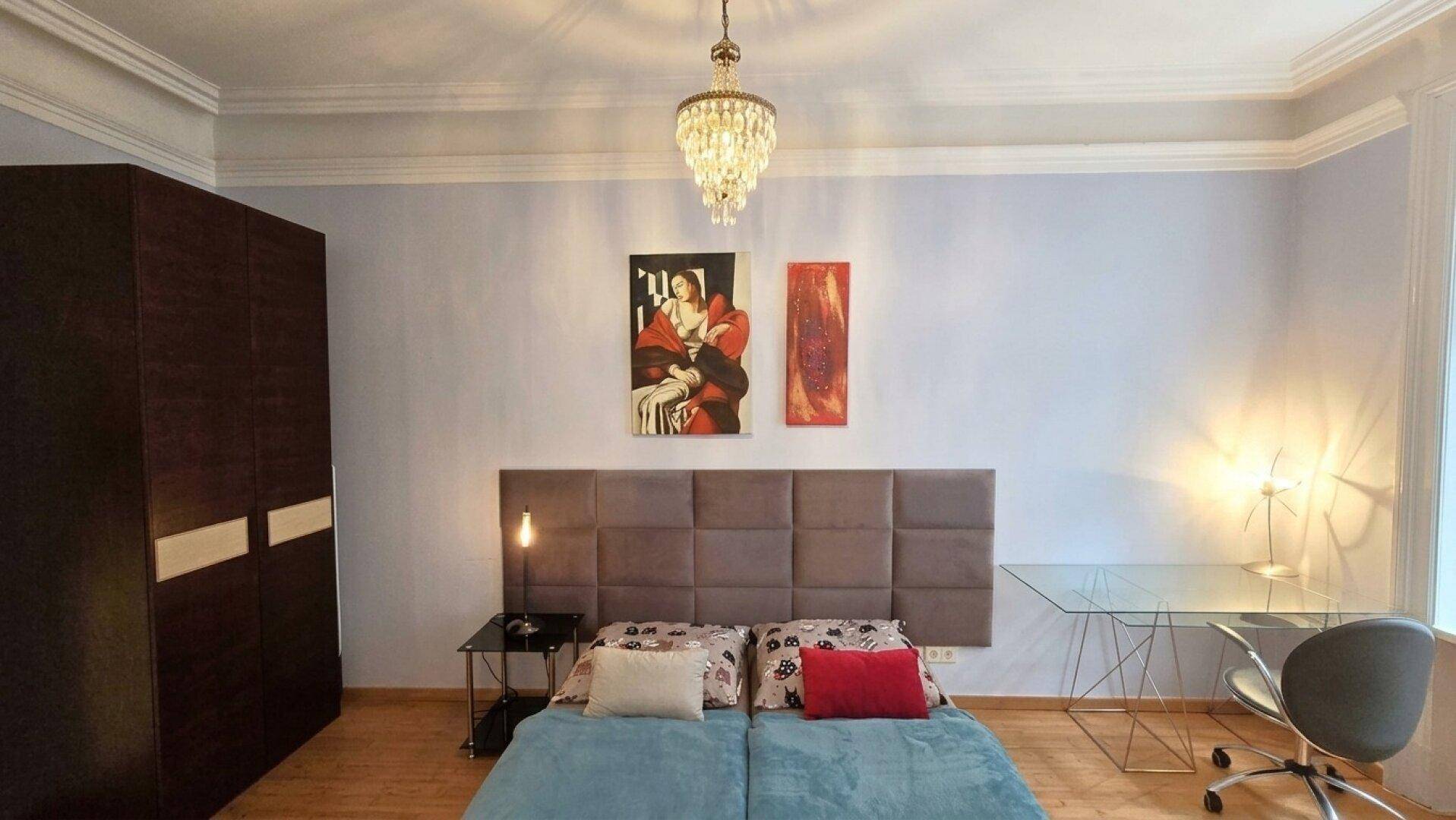 Schlafzimmer mit Holzboden, Kronleuchter und modernem Kopfteil.
