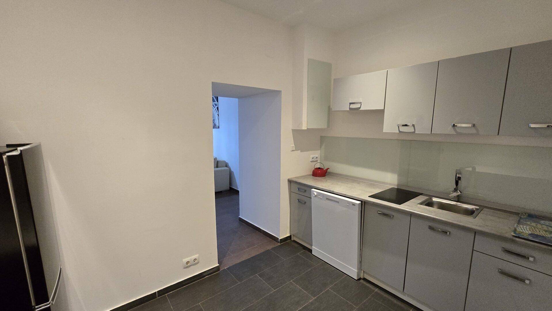 Funktionale Küche mit grauen Schränken, Kühlschrank, Geschirrspüler und Kochfeld, offen zum Wohnbereich.