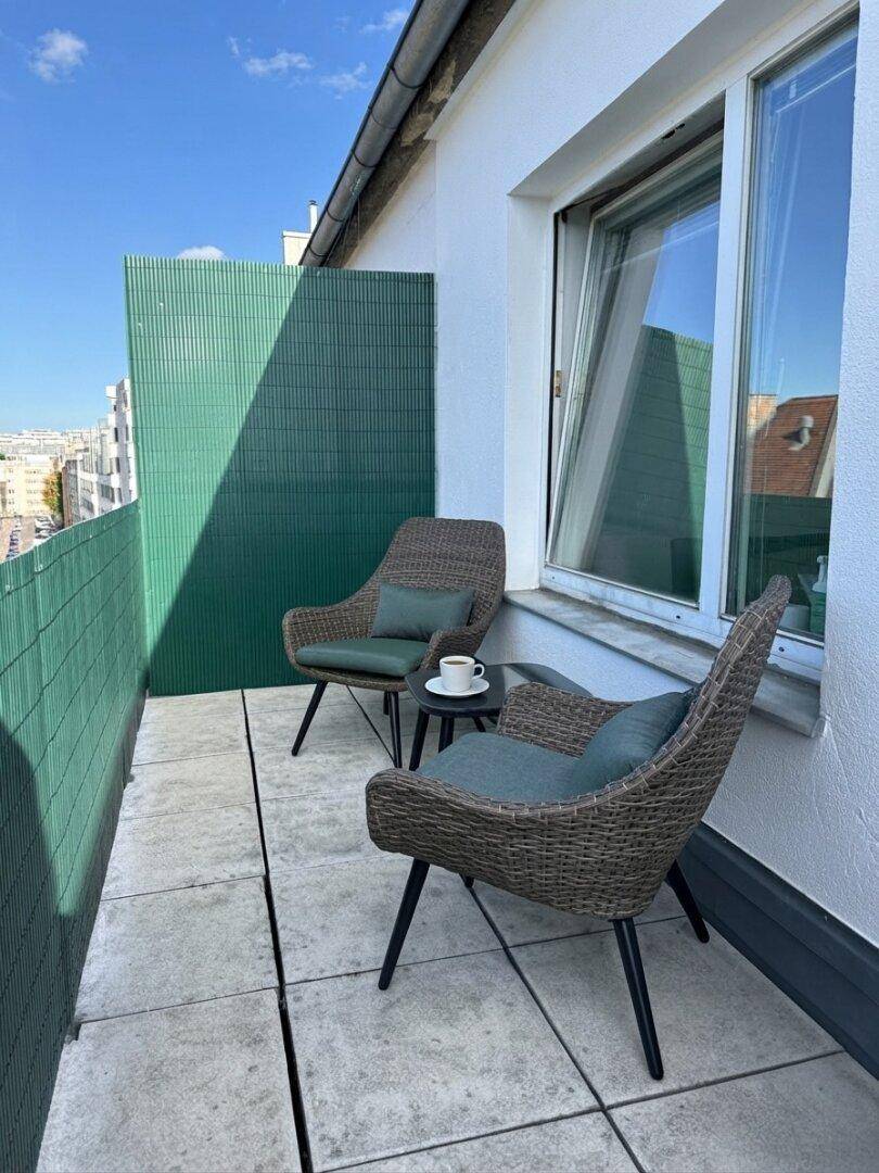 Gemütlicher Balkon mit Sitzgelegenheiten und Blick auf die Stadt unter blauem Himmel.