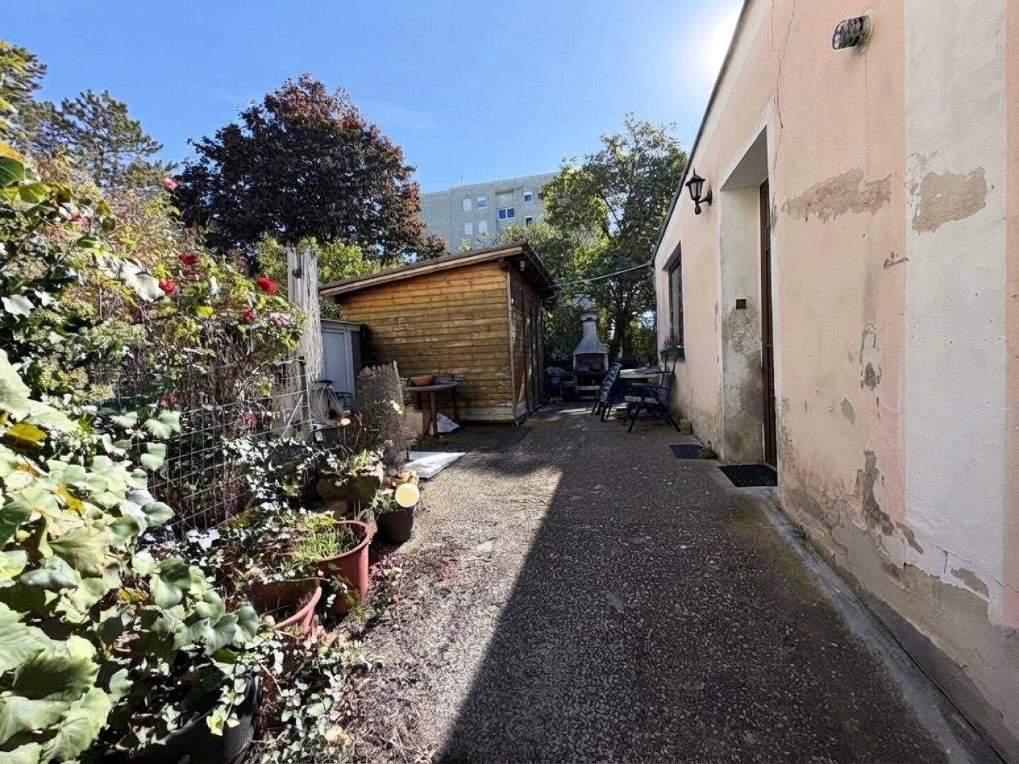 Schmaler Gartenweg führt zu einem Holzschuppen und einem Grillplatz mit vielen Pflanzen.