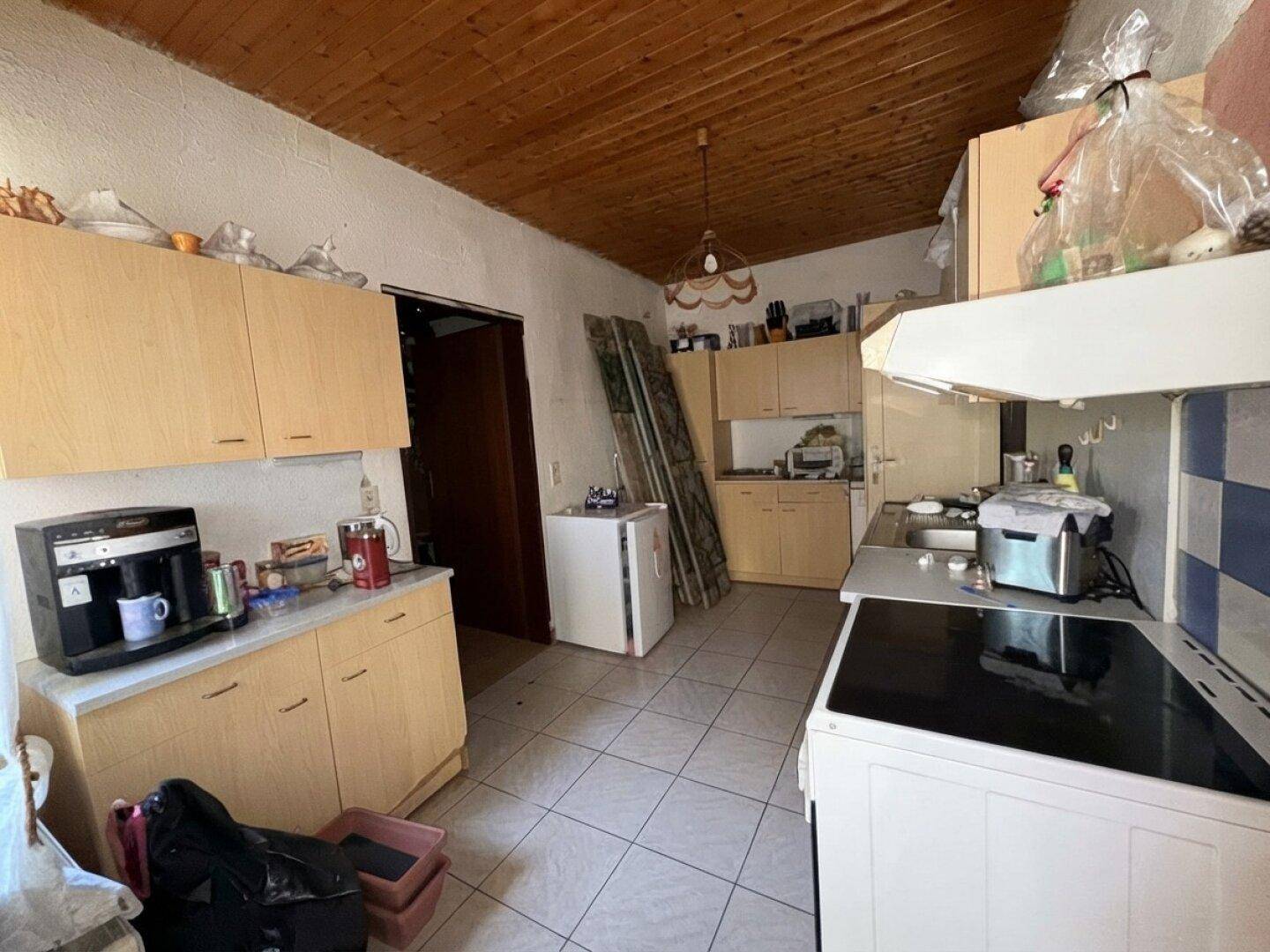 Einfache Küche mit Holzschränken, Fliesenboden und älteren Geräten, die eine Modernisierung benötigt.