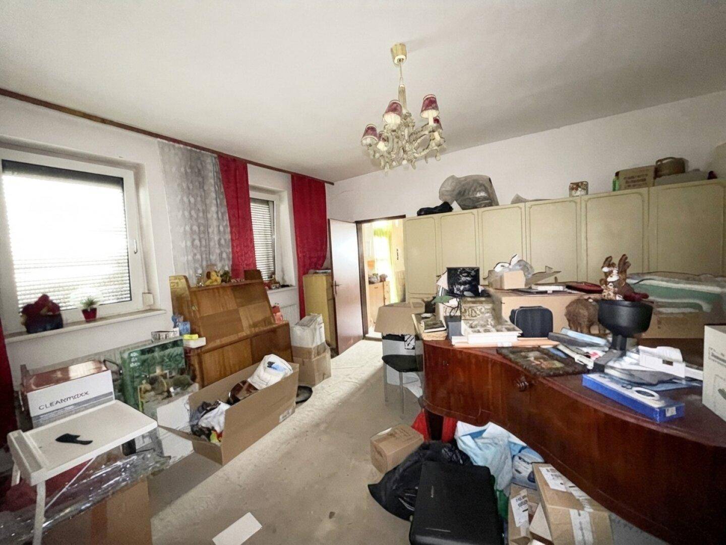 Helles Wohnzimmer mit Klavier, Schränken und vielen persönlichen Gegenständen, die auf eine Nutzung hindeuten.