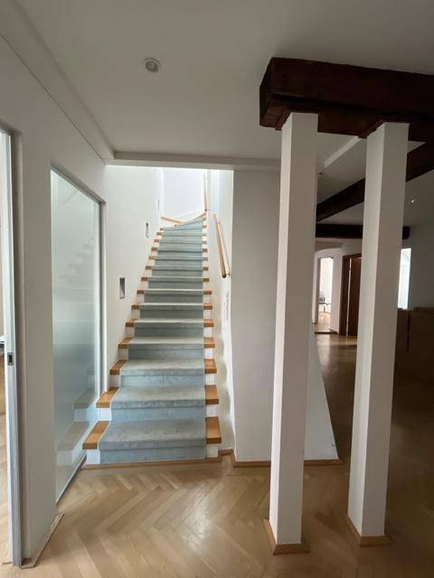 Elegante Treppe mit hellgrauem Teppich und Holzstufen, umgeben von Fischgrätparkett und Holzbalken.