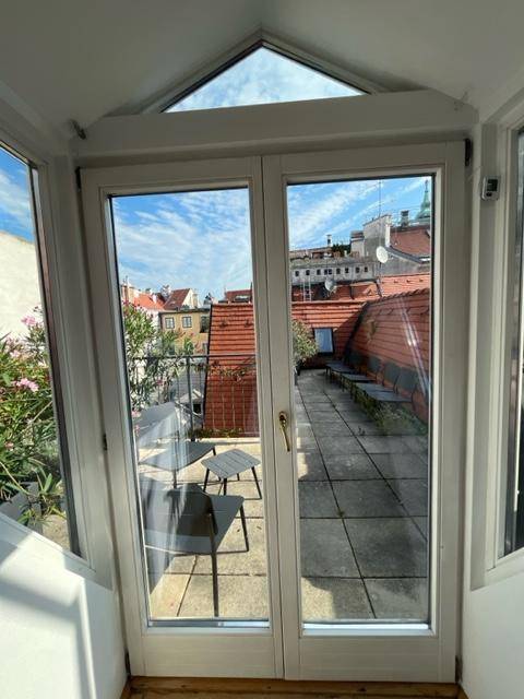 Terrasse mit Blick über die Dächer der Stadt, ausgestattet mit Gartenmöbeln unter blauem Himmel.