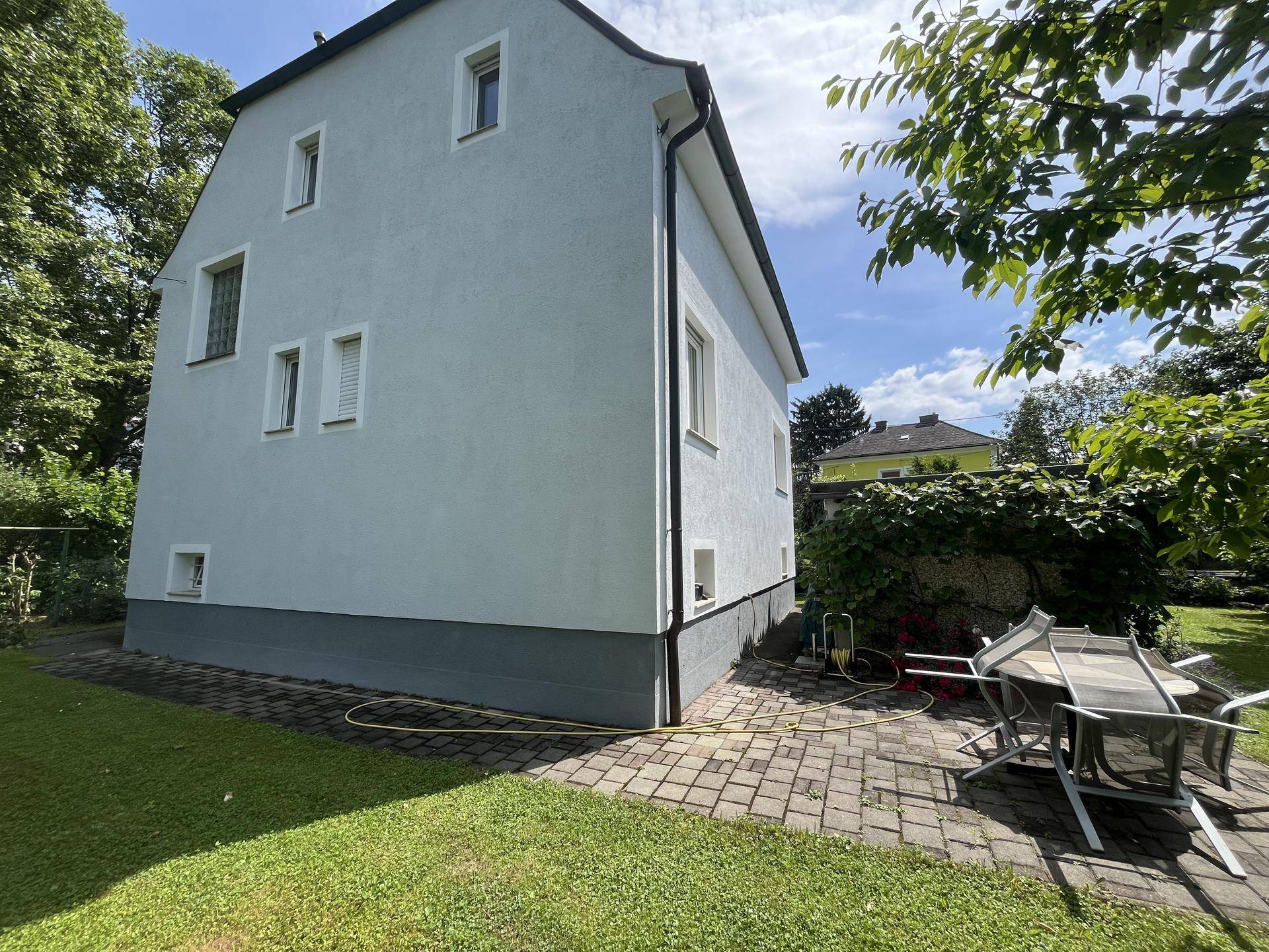 Seitliche Terrasse mit Gartenmöbeln und Zugang zum Rasen, umgeben von viel Grün.