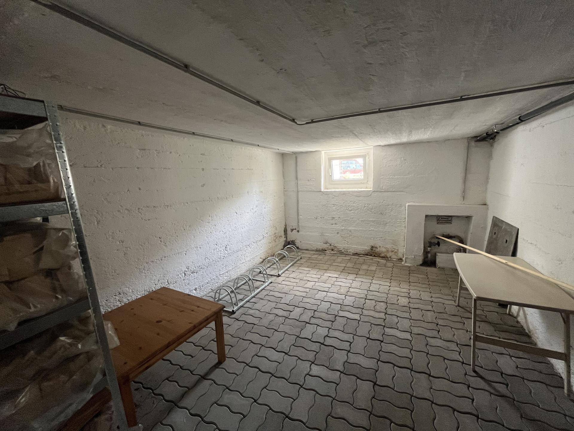 Geräumiger Kellerraum mit Betonwänden, Fliesenboden und kleinem Fenster für Belüftung.