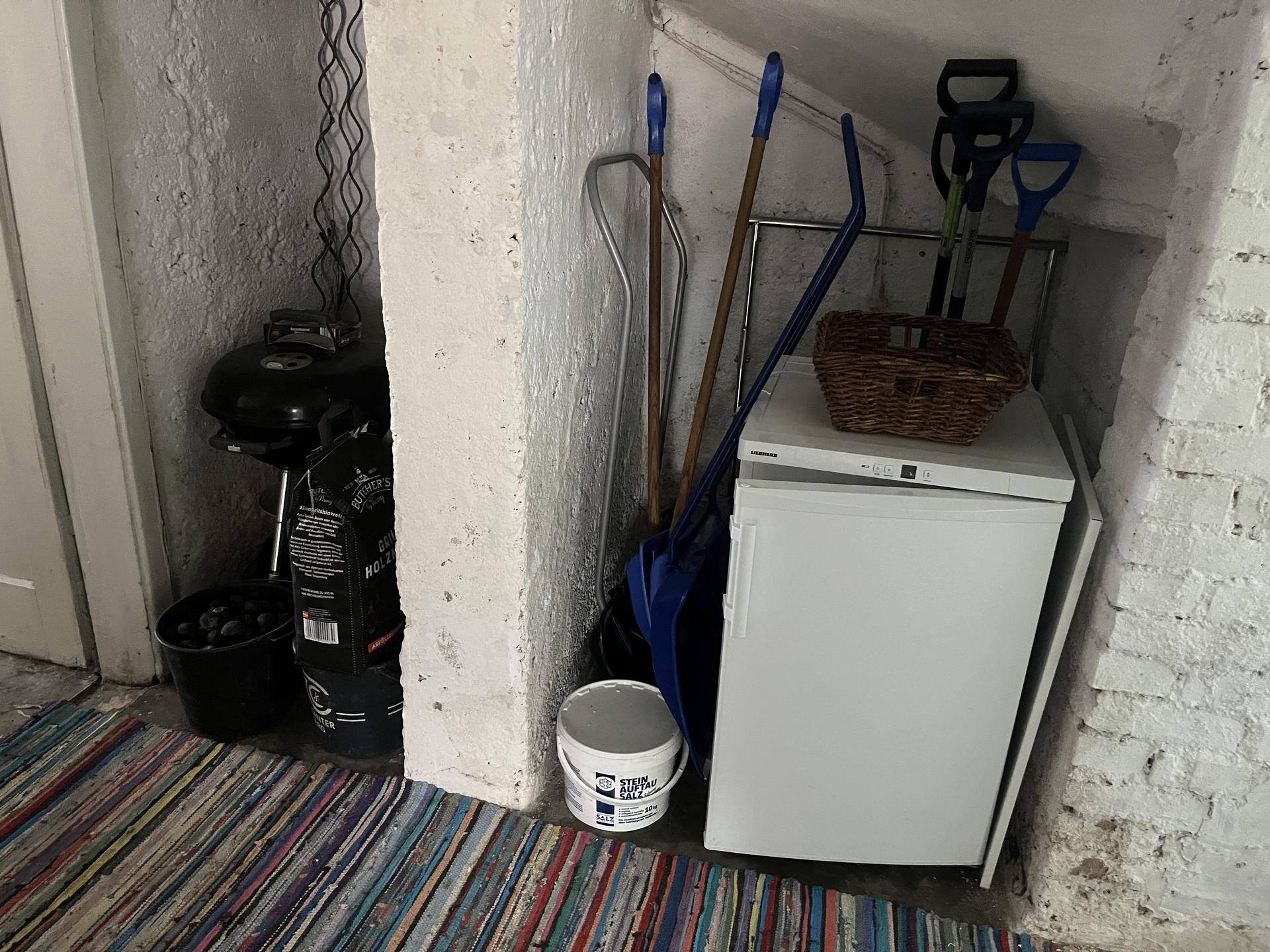 Praktischer Abstellraum im Keller mit kleinem Kühlschrank und Reinigungsutensilien.